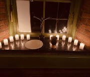 Eine Fensterbank, die mit brennenden Kerzen, einem Kelch und einem kleinen baumähnlichen Ornament dekoriert ist, schafft eine warme und gemütliche Atmosphäre in der Nacht.